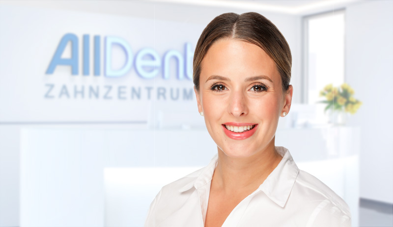 Freundliche Zahnärztin lächelt in die Kamera, im Hintergrund der Empfangsbereich der Praxis